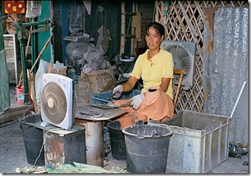 Chinese woman smelts computer circuit boards over an open stove to extract metals. The fan is an attempt to disperse the highly toxic fumes created by the smelting. 